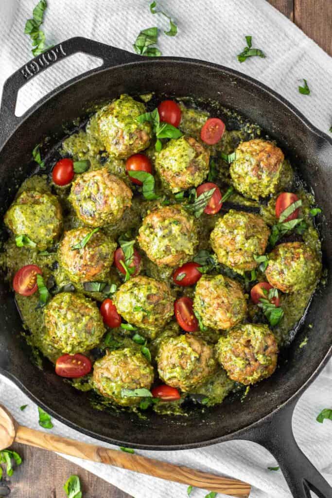 chicken pesto meatballs with grape tomatoes in a cast iron skillet.