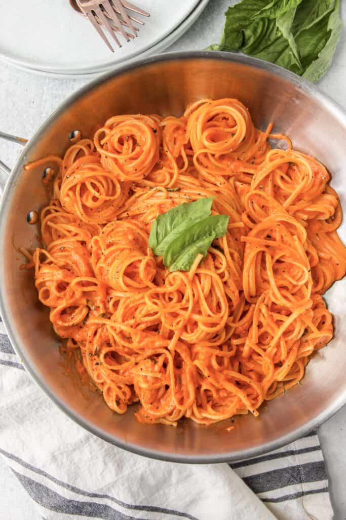 overhead photo of all the linguini in the stainless steel pan, plates and forks off to the side and a greyish and white napkin.