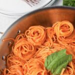 spiraled linguini in a creamy roasted red pepper sauce with white places and 2 copper forks