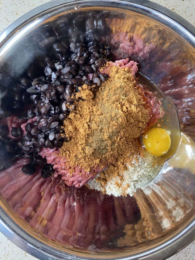 overhead shot of the bowl with all the ingredients. Ground beef, spices, beans, Panko, and egg.