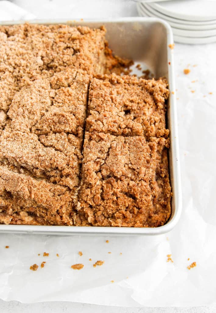 the coffee cake in the silver 8x8 baking pan, crumbs scattered about, plates in the background.