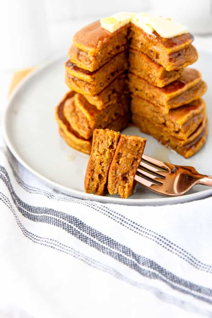 stack of pumpkin pancakes with a slice cut out, and two pieces of pancake on the fork.