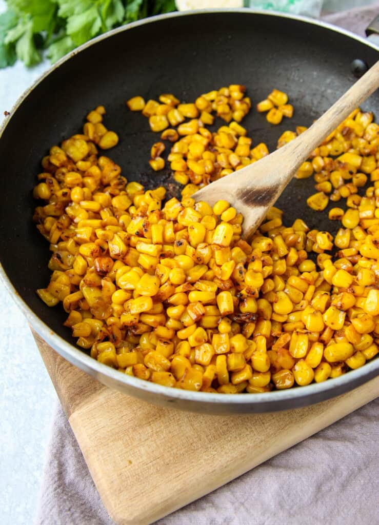 a pan of the pan roasted corn on a wood cutting board with a wood spoon.