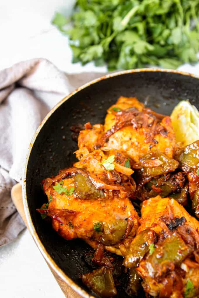 sazon chicken thighs in a black pan, a grey napkin and parsley in the back.