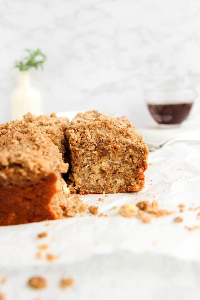 showing the inside of one of the slices of banana coffee cake with crumbs, a cup of coffee in the back.