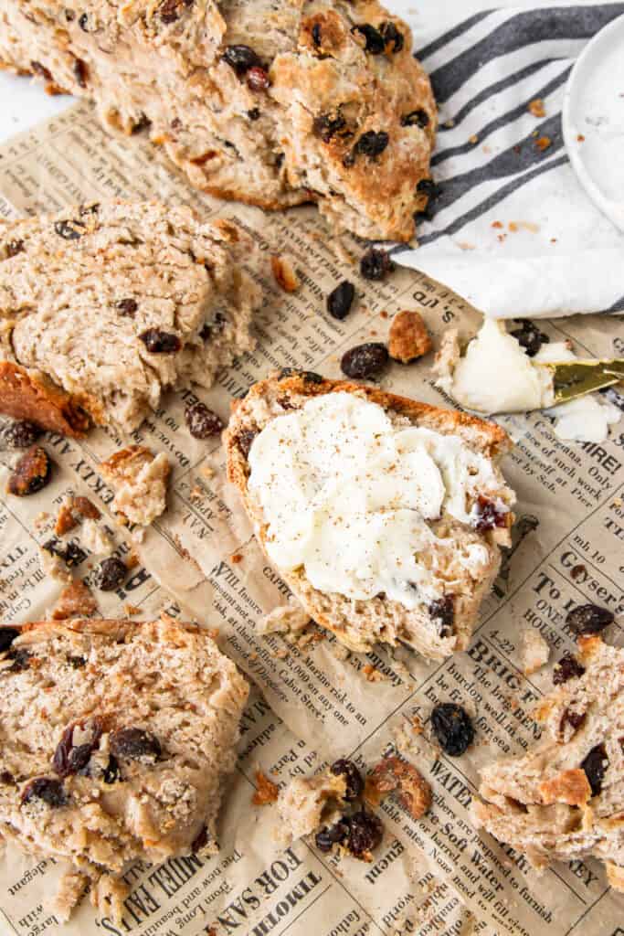 overhead shot of a slice of cinnamon raisin soda bread with butter on brown newsprint paper with raisins and crumbs