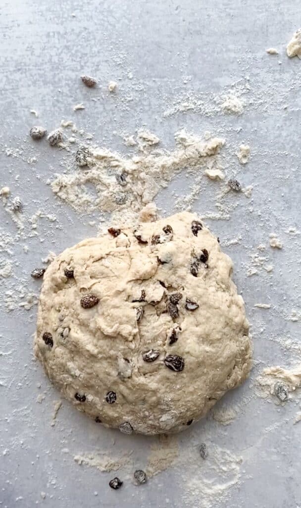 overhead shot of the unbaked dough on a grey cement surface with flour and raisins scattered about.