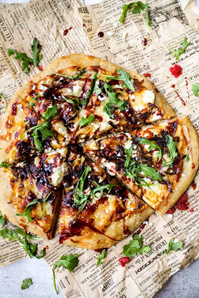 overhead shot of goat cheese and onion pizza on brown newsprint paper.