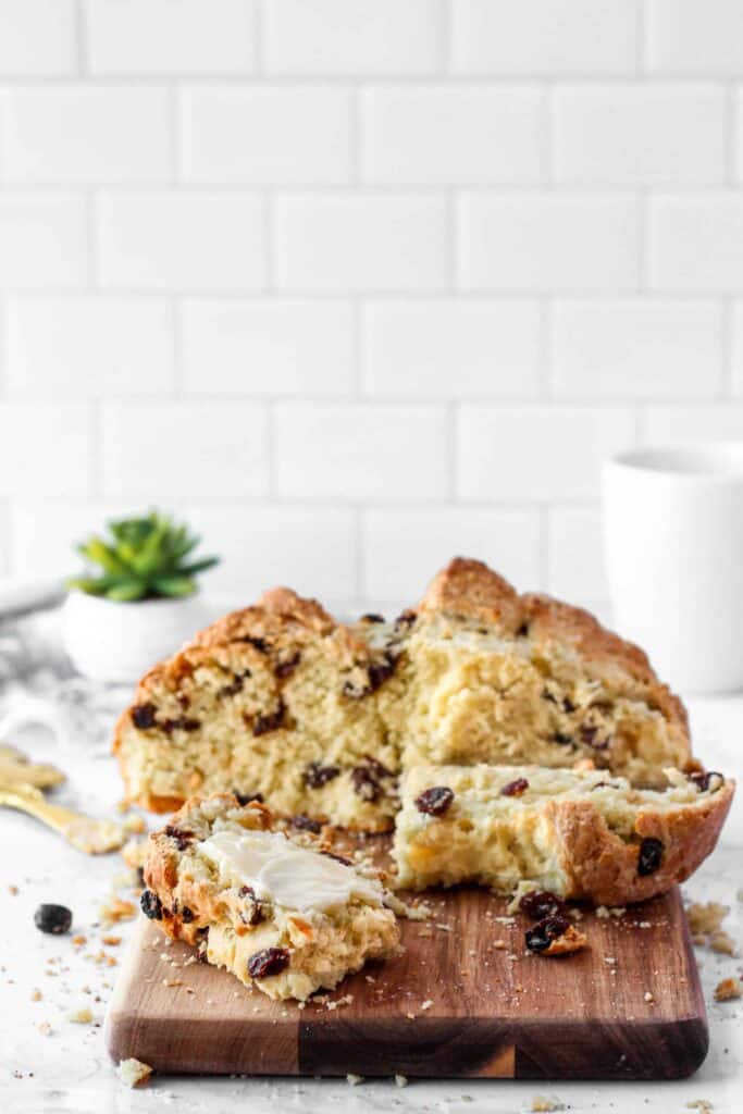 sliced Irish soda bread on a wood cutting board. White tile background with a white mug and green succulent. 