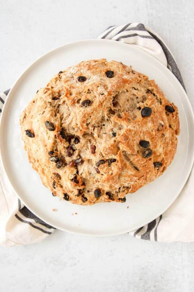 overhead shot of cinnamon raisin soda bread on a white round plate and a greyish striped napkin.