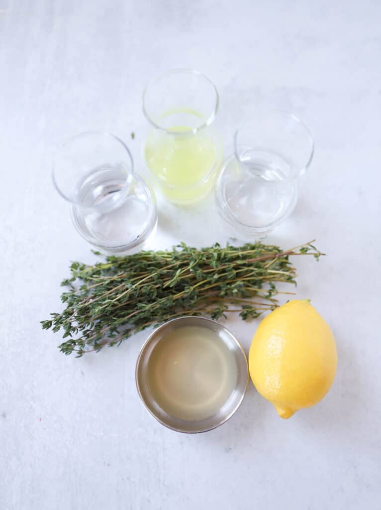 overhead shot of the limoncello martini ingredients: vodka, triple sec, limoncello, thyme, lemon juice, a lemon