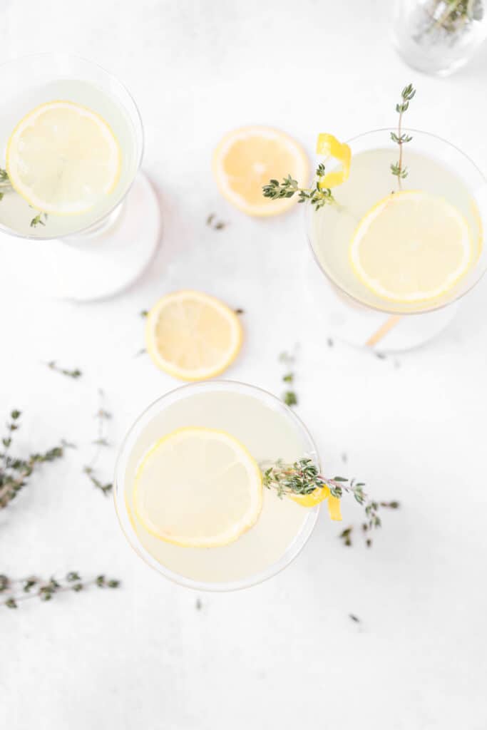 overhead shot of 3 of the martinis with lemon slices and thyme sprigs scattered around.