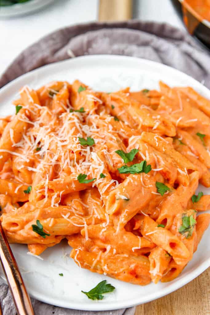 close shot of the penne vodka on the white plate on a wood board with a rose gold fork in close view.