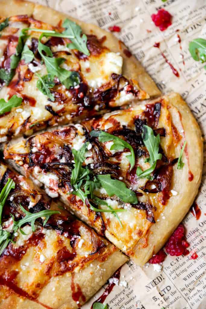 a slice of the goat cheese and onion pizza on brown newsprint paper with crushed raspberries.