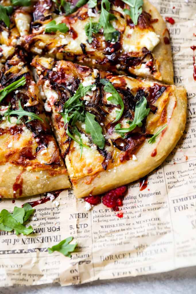 close shot of the goat cheese and onion pizza with raspberry balsamic on brown newsprint paper.