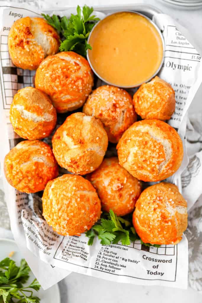overhead shot of the spicy pretzel bites on newsprint food paper with a beer cheese and parsley.