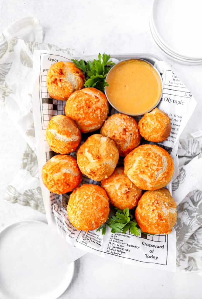 overhead shot of the tray of spicy pretzel bites on newsprint paper with plates and a dish of beer cheese.