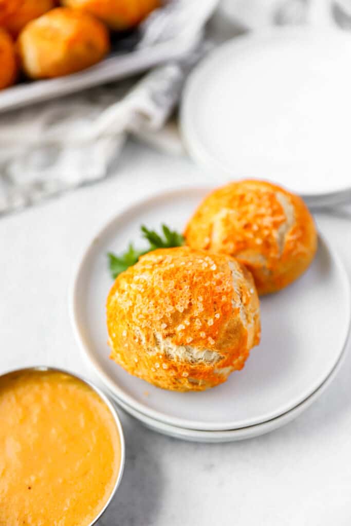 Two of the spicy pretzel bites on white plates with a dish of the beer cheese close to the camera.