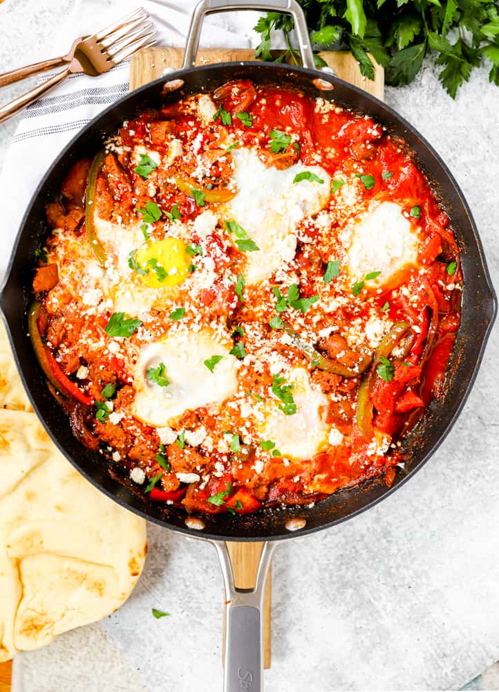 overhead shot of the finished shakshuka in the pan topped with queso freco and parsley, two forks off the the side.