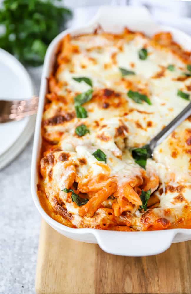 angled shot showing the corner of the casserole dish with the baked penne vodka on a wood board.