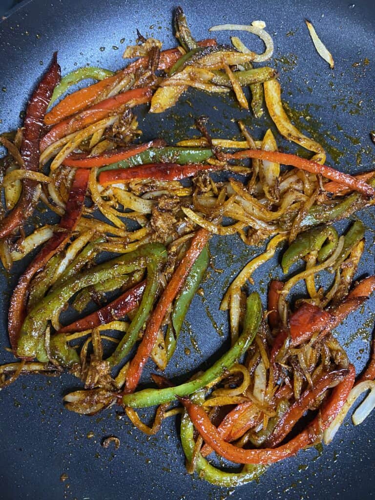 the peppers and onions in the pan coated with the spice mix.