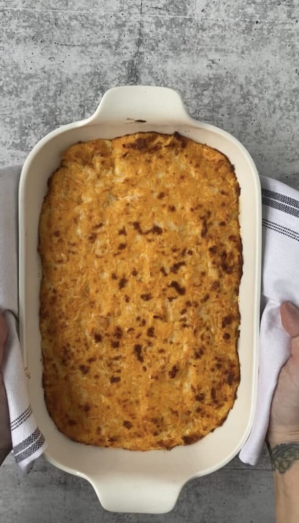 the baked buffalo chicken dip mixture in the white casserole dish, browned cheesy top.