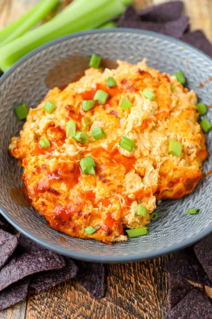 the buffalo chicken dip in a grey bowl topped with scallions and extra hot sauce.