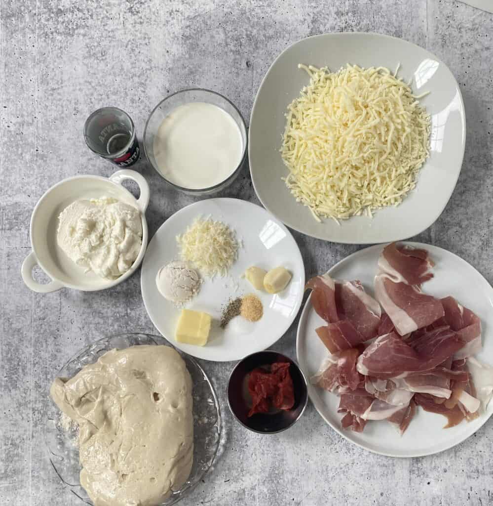 overhead shot of the ingredients vodka, cream, Mozzarella, ricotta, Parmesan, garlic powder, salt, pepper, flour, butter, prosciutto, tomato pasta, pizza dough, garlic cloves.