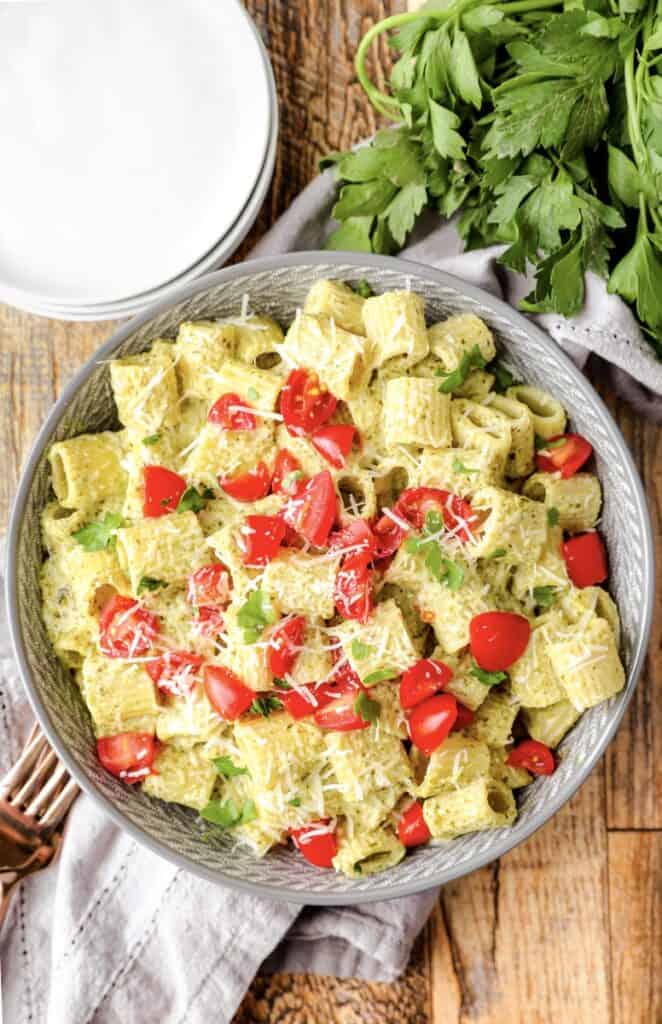 overhead shot of the pasta in a grey bowl on a wood surface, a grey linen, and parsley off to the side.