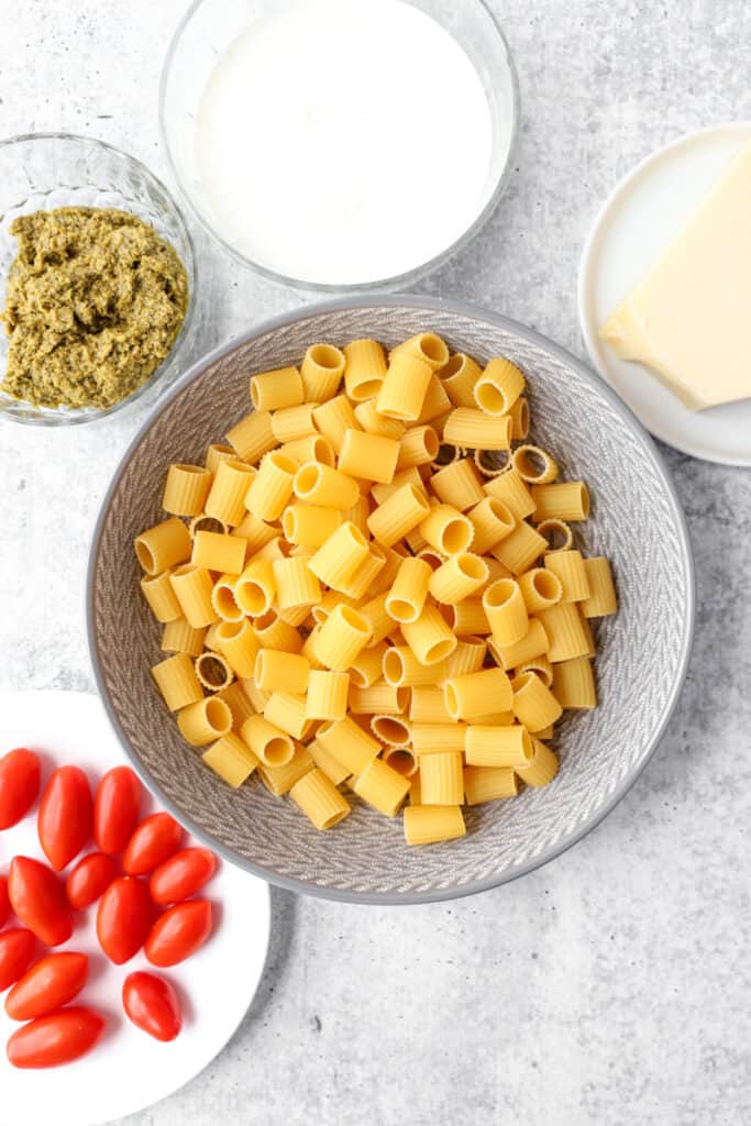 overhead shot of the ingredients: mezzi rigatoni, cherry tomatoes, Parmesan cheese, pesto, cream.