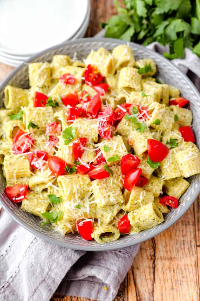 close shot of the pasta in a grey bowl with a grey linen napkin and parsley bunch in the background.