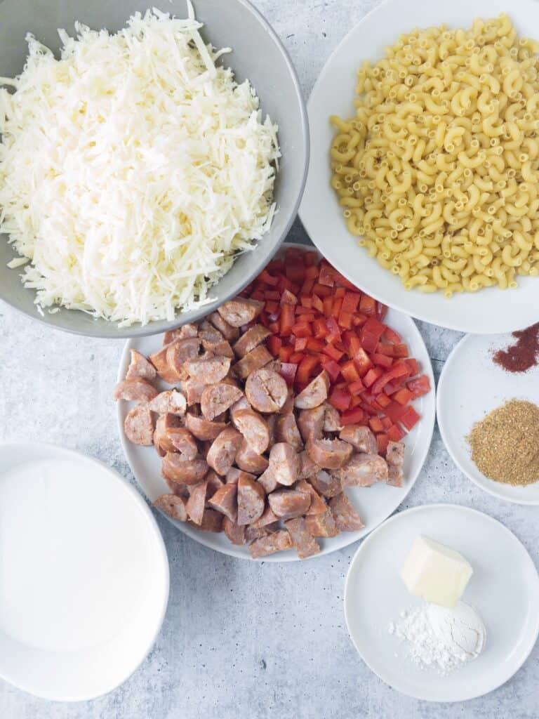 overhead shot of the ingredients. White Cheddar, macaroni noodles, andouille sausage, red peppers, cream, butter, flour, Cajun seasoning, smoked paprika, salt. 