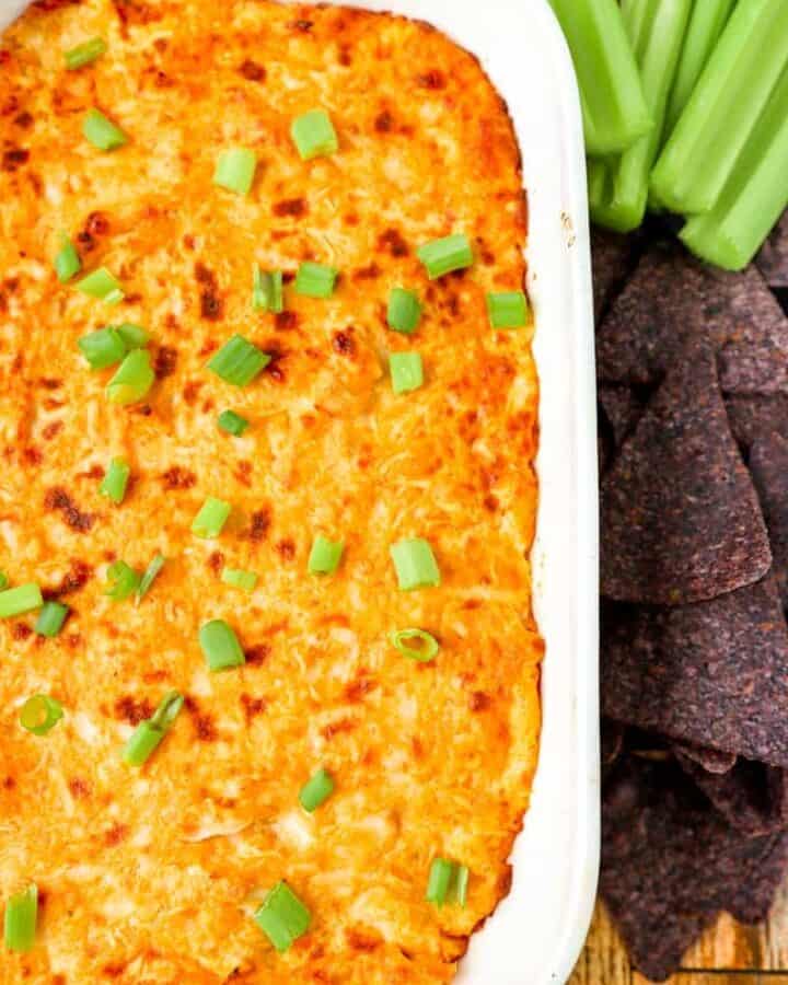 buffalo chicken dip in a white dish with blue corn tortilla chips and celery