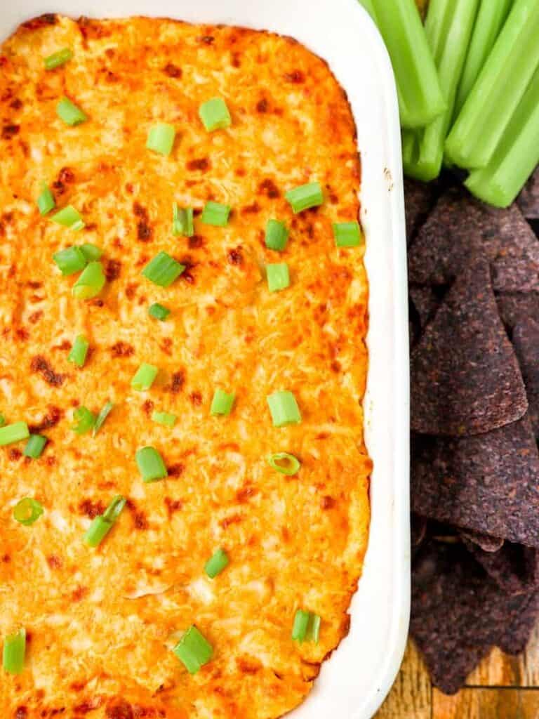 buffalo chicken dip in a white dish with blue corn tortilla chips and celery