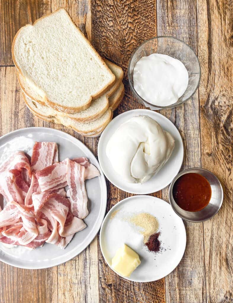 overhead shot of the ingredients on a wood surface: bread, crema, Oaxaca, raw bacon, adobo sauce, garlic powder, salt, chili powder, butter.