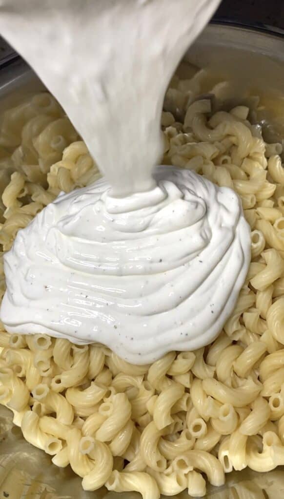 pouring the dressing onto the cooked noodles.