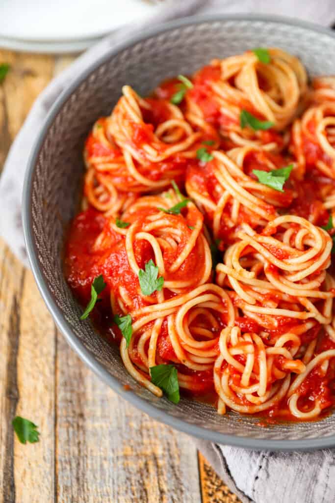 close photo of the spaghetti covered in the sauce in pasta spirals in a grey bowl on a wood pattern surface.