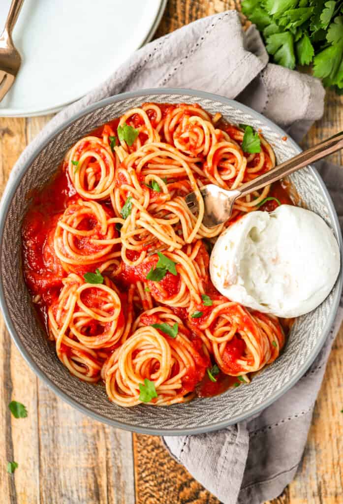 overhead photo of the bowl of spaghetti with a fork and a large ball of Burrata cheese.