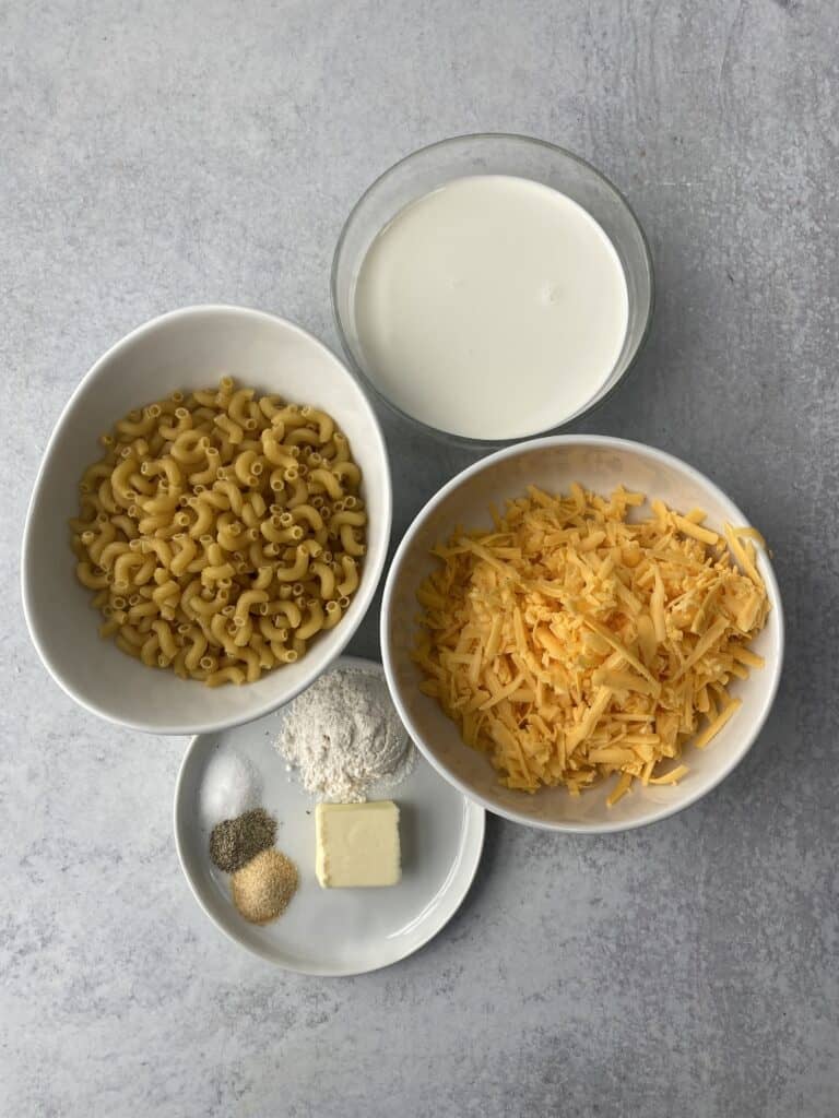 overhead shot of the ingredients: macaroni, cream, shredded Cheddar cheese, butter, flour, salt, pepper, garlic powder.