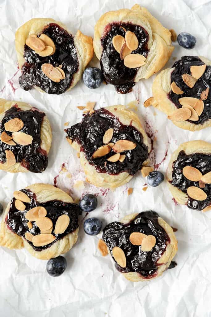 overhead shot of several of the blueberry Danishes on parchment paper with blueberries scattered about.