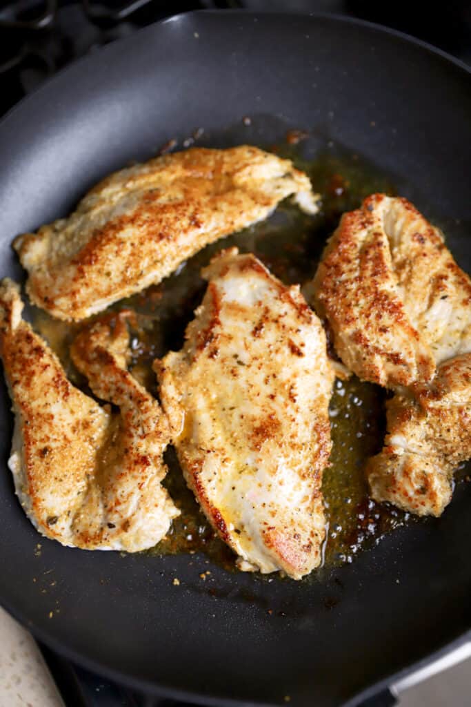 4  Cajun seasoned chicken breasts cooking in a black pan.