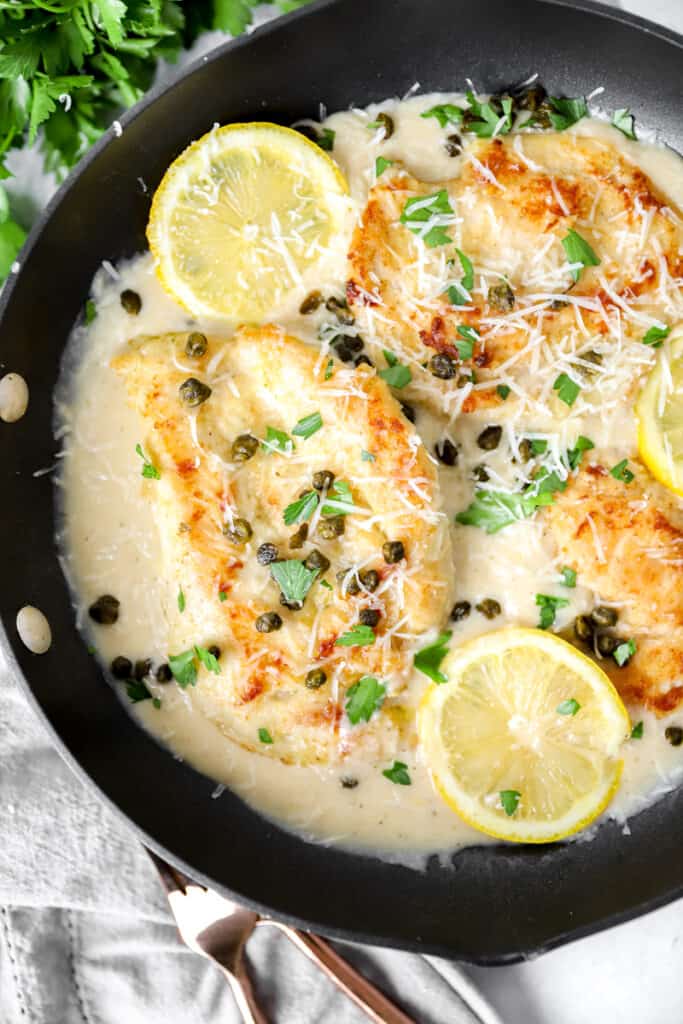 overhead shot of the creamy chicken piccata in a pan with lemon slices.