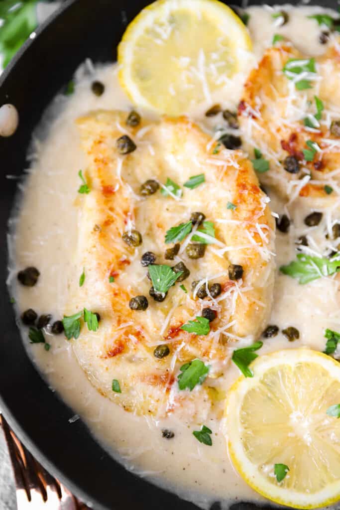 close shot of one of the chicken breasts in the pan with piccata sauce and fried capers. 