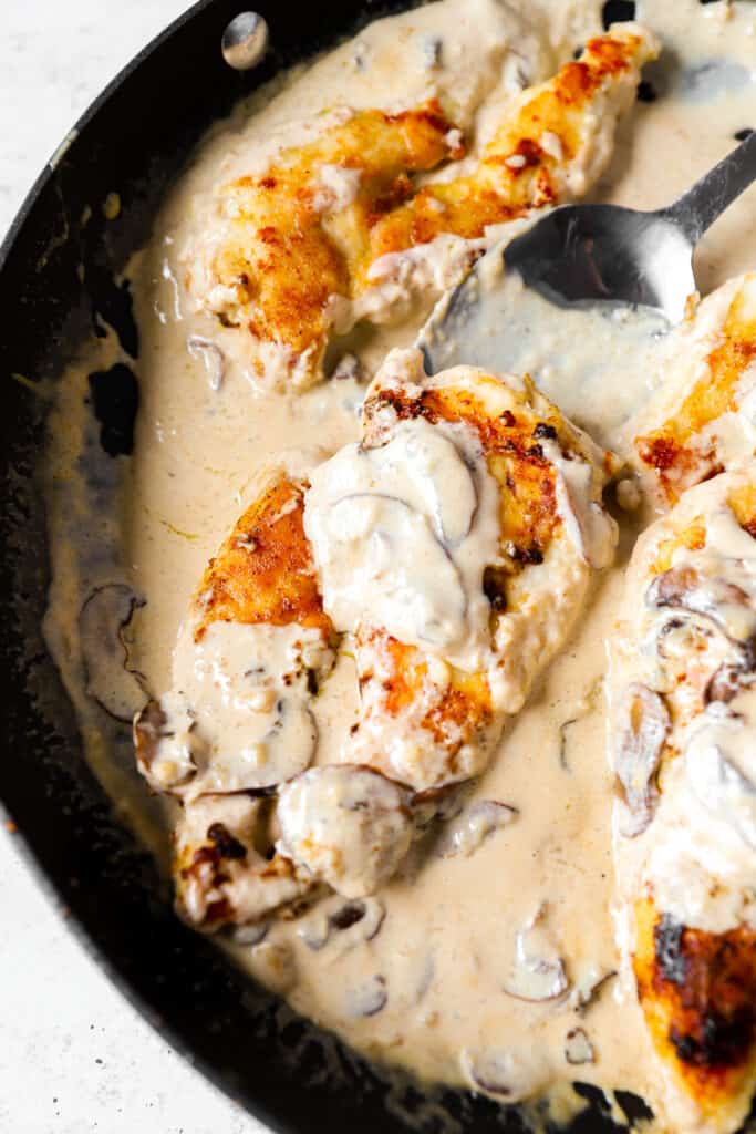 overhead shot of the creamy chicken marsala in a black pan with a silver spoon