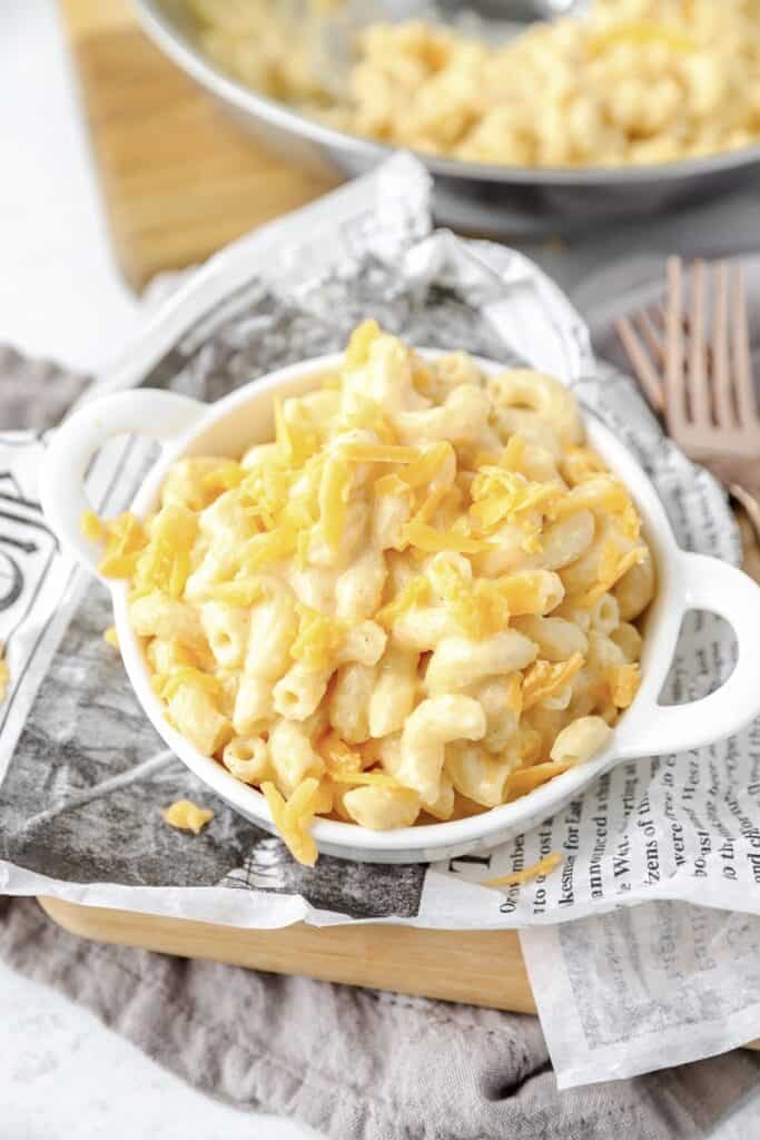 angled shot of the mac and cheese in a white dish on newsprint paper and two copper forks.