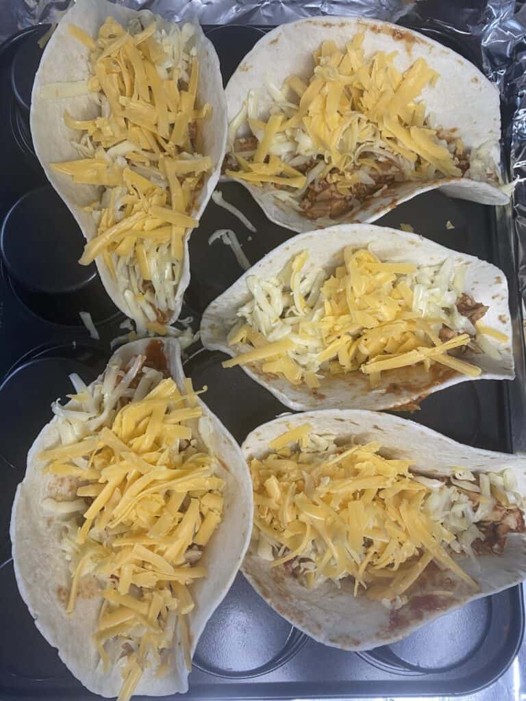 overhead shot of the tacos in the muffin pan, filled with the chicken mixture and cheeses.