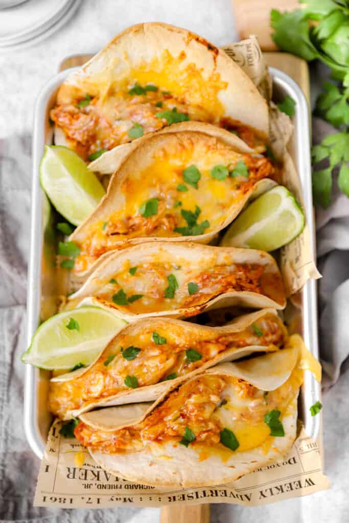 overhead shot of the oven baked chicken tacos in a silver platter with lime wedges.