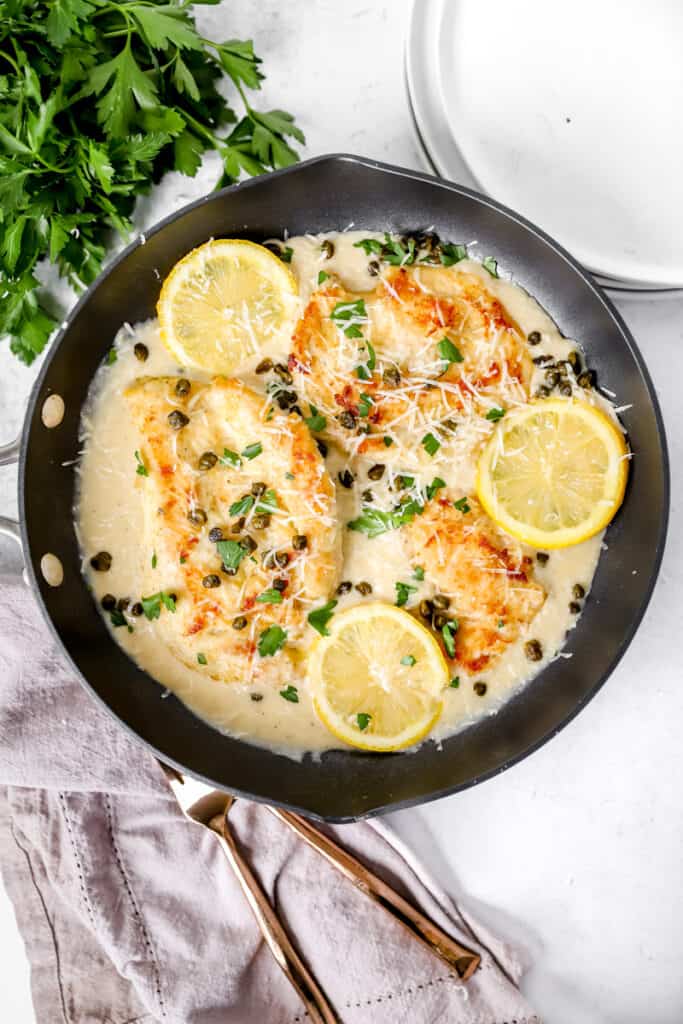 overhead shot of the creamy chicken piccata in a pan with lemon slices with parsley in the background.