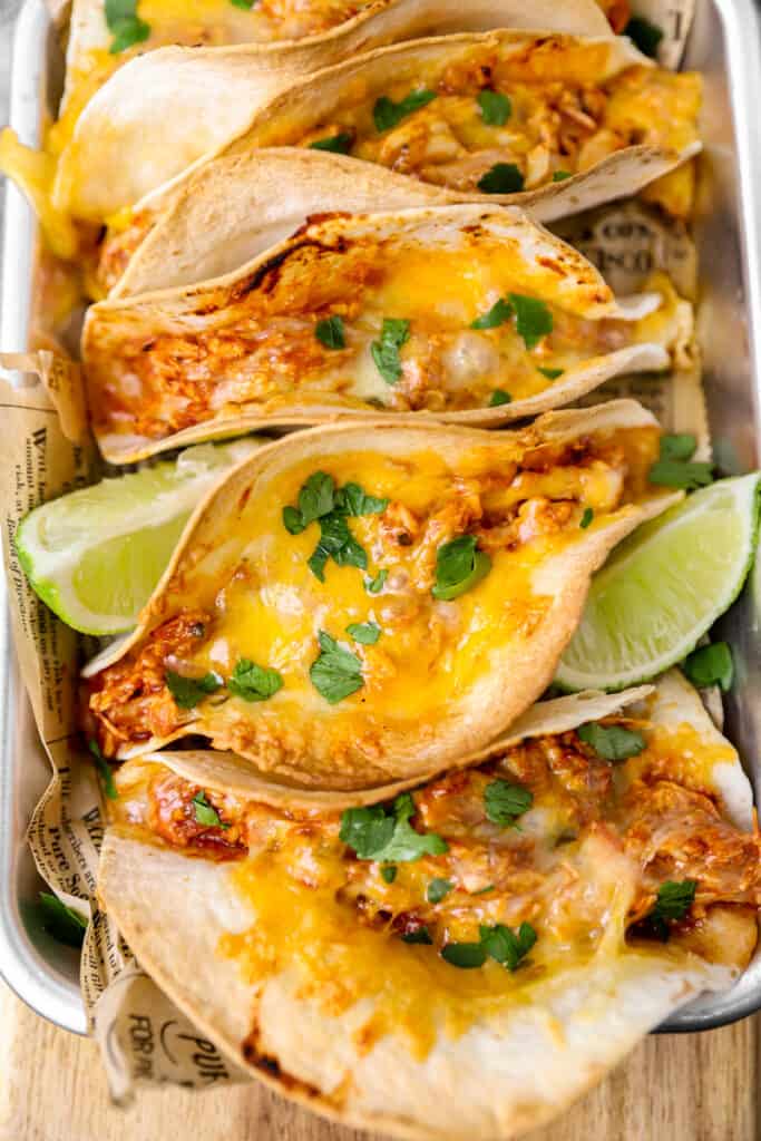 overhead shot of the tacos showing lots of melty cheeses, topped with parsley and lime wedges.