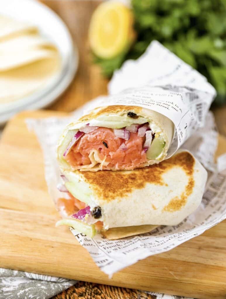 smoked salmon wrap on a wood board, tortillas and parsley in the background.